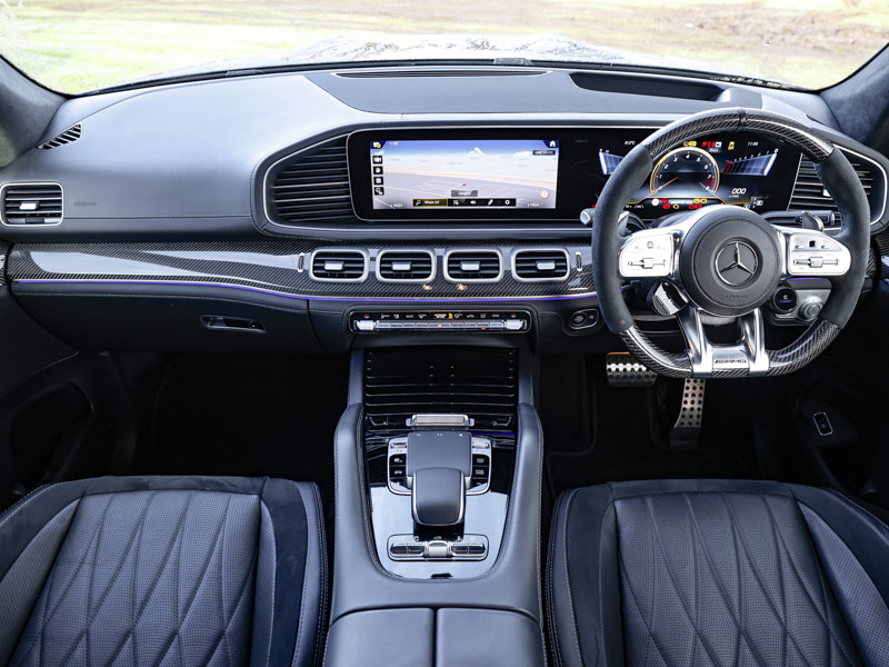 Inside the Mercedes-Benz GLS cockpit, showing the steering wheel, dashboard, centre console, infotainment screen and front seats