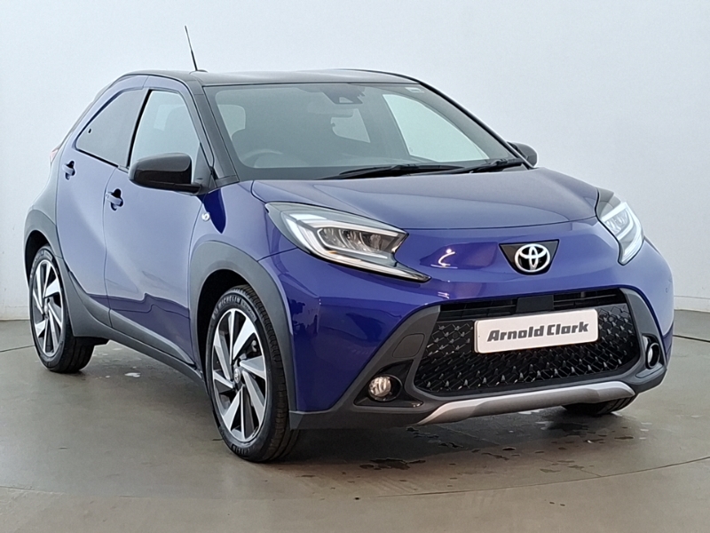 A blue Toyota Aygo X parked from the front on a grey background